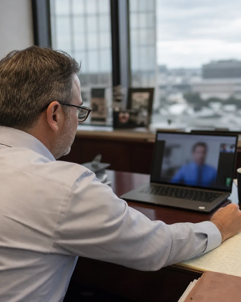 Audit manager on a video call with a software sales rep, notepad with seat counts beside the laptop