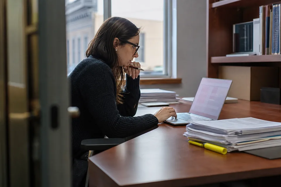 Audit senior matching sampled invoices to a spreadsheet on a laptop beside a stack of client documents