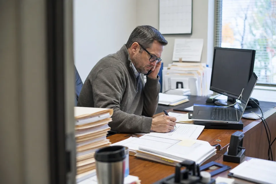 Senior accountant at a small CPA firm working through a stack of compilation files beside a desk calendar marked for year end